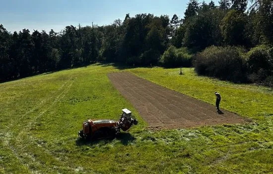 Luftaufnahme einer frisch bearbeiteten Bahn auf einer Wiese am Waldrand