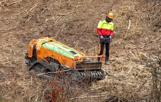 Bediener steuert eine Funkraupe mit Forstmulcher aus sicherer Entfernung über eine Rodungsfläche