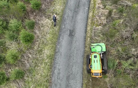 Luftaufnahme einer Funkraupe beim Mähen des Bankettstreifens entlang eines Weges