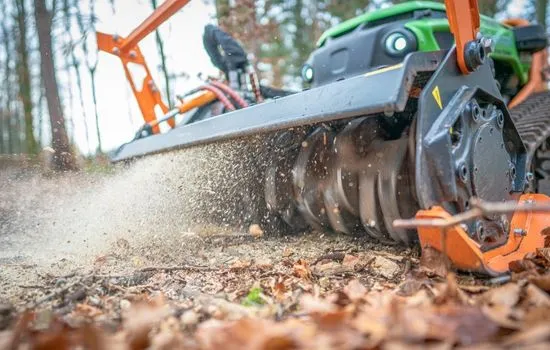 Mulchrotor im Einsatz, aufgewirbeltes Laub und Häckselgut über dem Waldboden