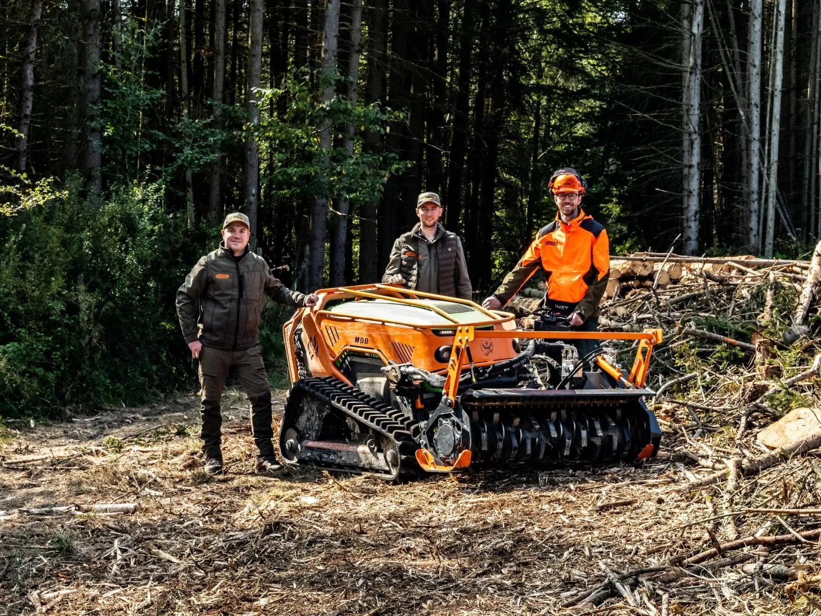 Das Team von KSK-Vermietung mit einer orangefarbenen MDB Funkraupe auf einer Forstfläche